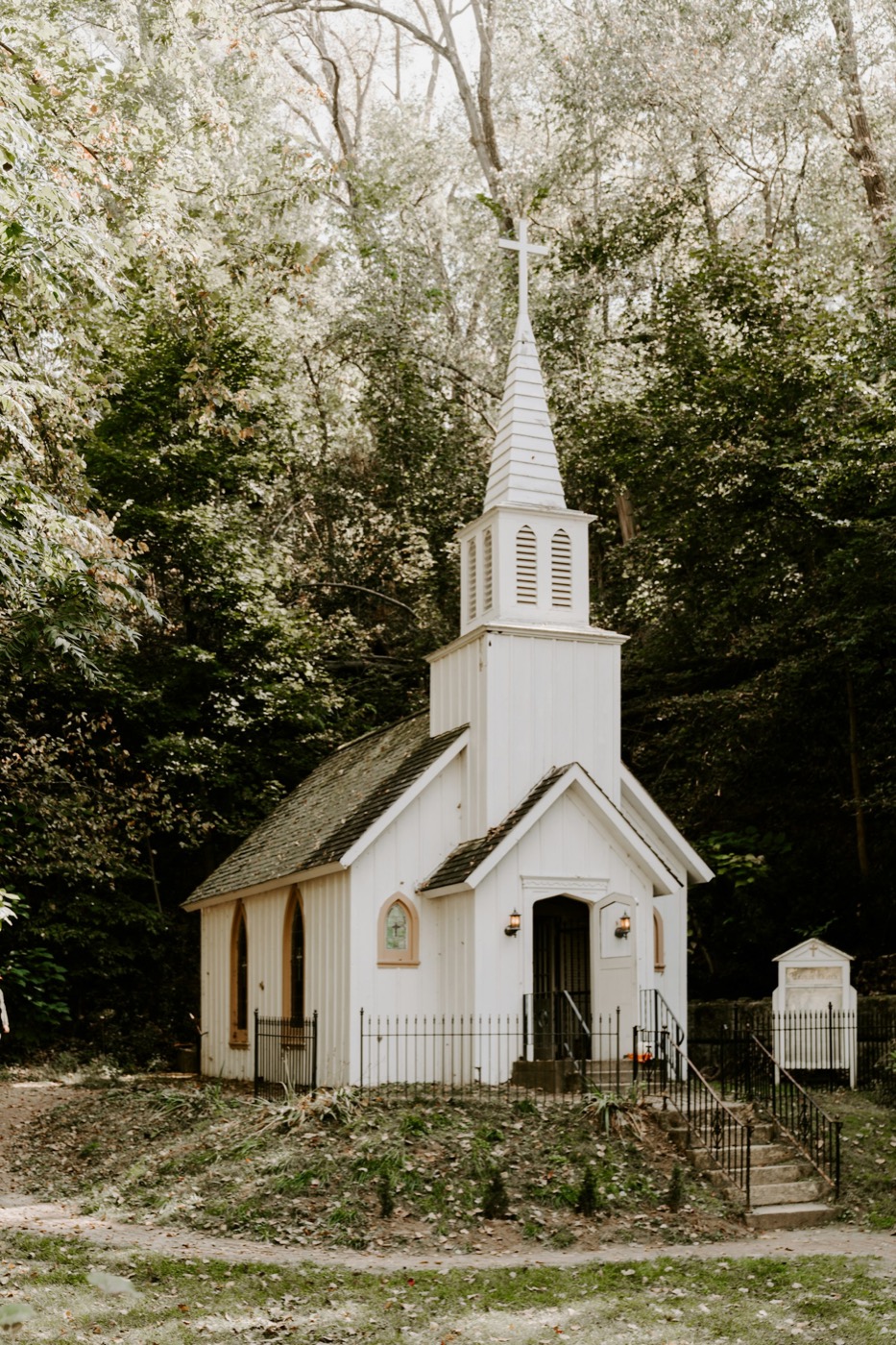A small white chapel with a steeple among green trees