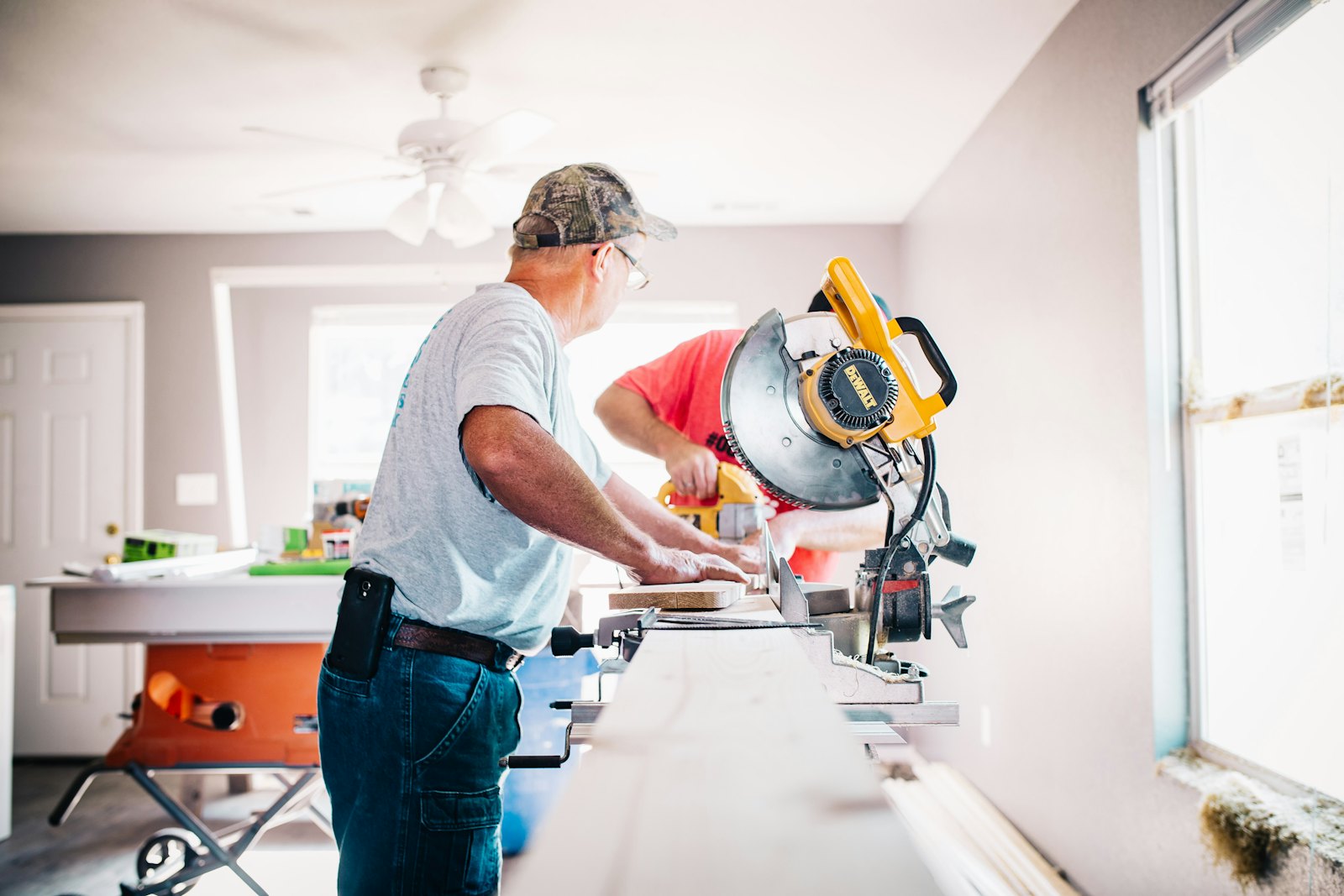 Two contractors cutting trim on a saw inside a house they are finishing